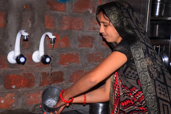 Indian rural housewife washes utensils in the kitchen with tap water. brick wall background