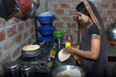 Hintli kırsal bir ev hanımı LPG gazı, mutfak konsepti, yemek pişirme evi, tuğla duvar arka planı kullanarak toprak kabında (roti) ekmek pişiriyor.