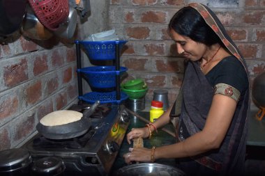 Hintli kırsal bir ev hanımı LPG gazı, mutfak konsepti, yemek pişirme evi, tuğla duvar arka planı kullanarak toprak kabında (roti) ekmek pişiriyor.