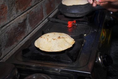 Hintli bir ev kadınının elleri, LPG gazı kullanarak toprakta ekmek pişirirken (chapati)
