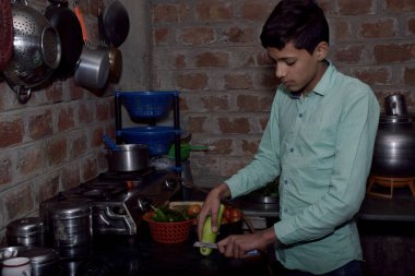 Hintli taşralı çocuk mutfakta kabak kesiyor, mutfak konsepti, tuğla duvar arka planı