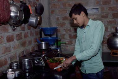 Hintli taşralı çocuk mutfakta domates kesiyor, mutfak konsepti, tuğla duvar arka planı