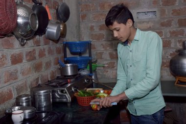 Hintli taşralı çocuk mutfakta domates kesiyor, mutfak konsepti, tuğla duvar arka planı