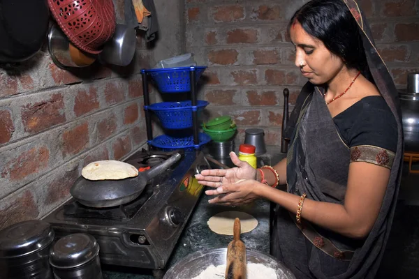 Hintli kırsal bir ev hanımı LPG gazı, mutfak konsepti, yemek pişirme evi, tuğla duvar arka planı kullanarak toprak kabında (roti) ekmek pişiriyor.