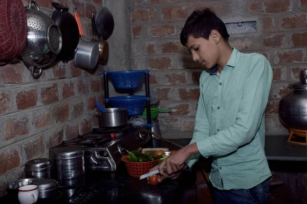 Indian rural boy cutting tomatoes in the kitchen, kitchen concept, brick wall background