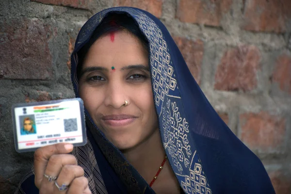 Indian rural woman wearing a sari with smiling face shows her blurred aadhar card in her hand, brick wall background