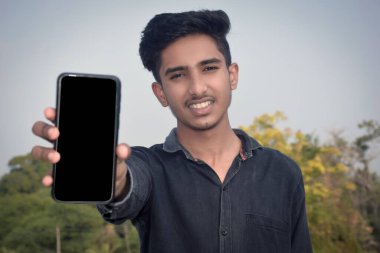 Siyah gömlek giyen bir öğrenci akıllı bir telefonun ekranını gösteriyor. Çocuğa odaklan. İdeolojik. Konumu Kopyala.