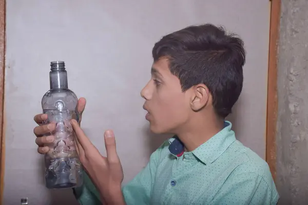 Asyalı genç çocuk plastik şişeden su içiyor, üzerinde siyah noktalı açık yeşil bir gömlek var.