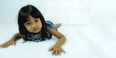 Beyaz arka planda uzanmış kameraya bakan küçük bir çocuğun portresi. Pozitif duygular.