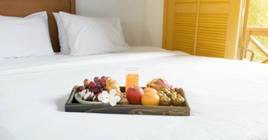 Breakfast, fruit, croissants, orange juice, in a black wooden tray, on a white bedsheet, Healthy food concept.