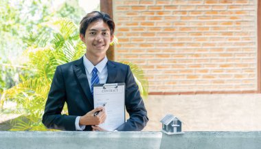 Emlakçı ev modelini tutuyor ve iş sözleşmesini, kirayı, ipoteği, krediyi ya da sigortayı açıklıyor.