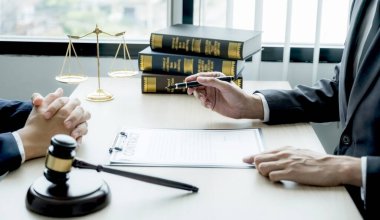 Avukatın eli kalem tutuyor ve ofisteki adama hukuki danışmanlık hizmeti veriyor. Adalet terazisi ve tokmak çekiciyle..