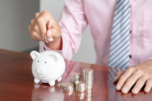Businessman hand putting coin into white piggy bank, step up start up business to success, Saving money for future plan and retirement fund concept