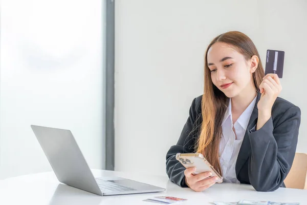 stock image Young consumer woman holding a credit card, Ready to spending pay online shopping according to discount products via smartphone and laptop from home.