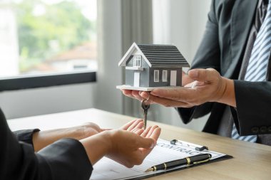 Emlakçı ev modelini tutuyor ve iş sözleşmesini, kirayı, satın almayı, ipoteği, krediyi ya da ev sigortasını alıcıya anlatıyor..