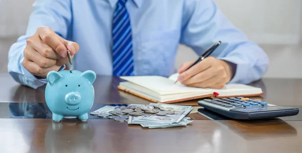 stock image Businessman hand putting coin into blue piggy bank, saving money for future investment plan and retirement fund concept.