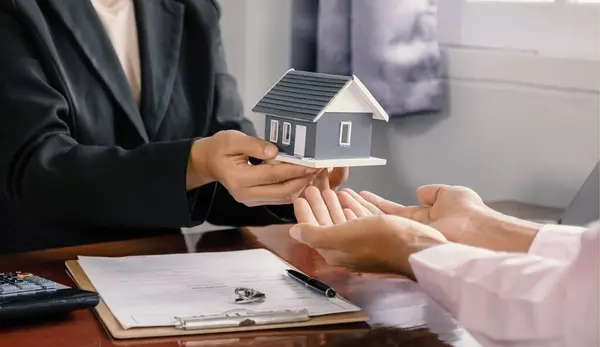 stock image Hand a real estate agent hold the home model, and explain the business contract, rent, buy, mortgage, loan, or home insurance to the buyer man