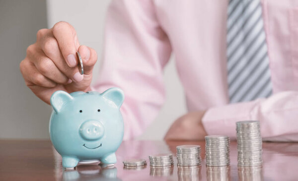 Businessman hand putting coin into blue piggy bank, step up start up business to success, Saving money for future plan and retirement fund concept