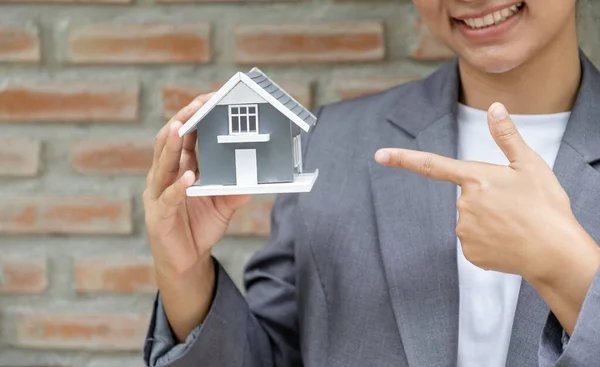 Real estate agent hands holding the home model stand in front of the red brick wall background or Sales presenting home insurance.