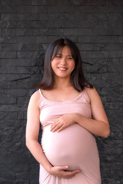 ドレスのママ妊娠中の女性は 黒いレンガの背景に腹に手を保持し 愛とあなたの赤ちゃんの誕生を待っています — ストック写真