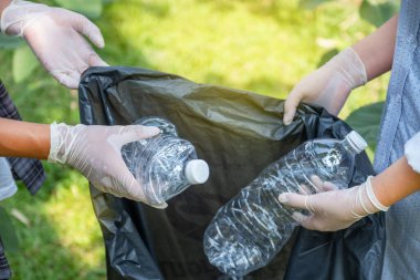 Ellerinde plastik şişelerle çöpleri toplayan çift, Dünya Çevre Günü 'nde Ayçiçeği Parkı' ndaki siyah çöp torbasına atıyorlar..