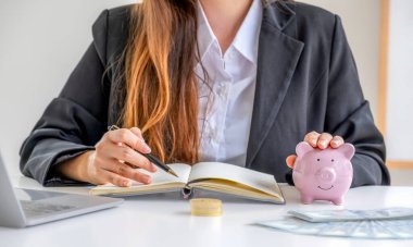 İşkadını yönetiminin elinde pembe kumbaralı kalem ve online pazarlama için dizüstü bilgisayarı kullan, işleri suşiye yükselt, gelecek planı ve emeklilik fonu konsepti için para biriktir.