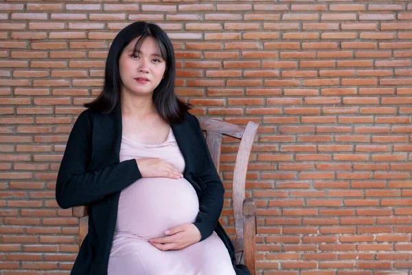 ドレスのママ妊婦は赤レンガの背景に腹に手を保持し 愛とあなたの赤ちゃんの誕生を待っています — ストック写真