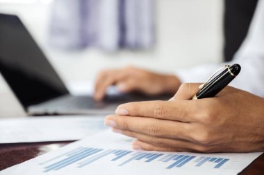 İş adamlarının ellerindeki kalem ve hesap makinesi, dizüstü bilgisayar analizi zorlu iş hedefleri belirleme grafiği ve merkez ofisindeki hedefe ulaşmaya hazır..