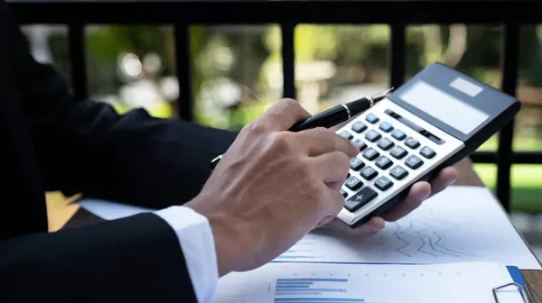 Businessmen bookkeeper hand holding pen and use calculator, laptop analysis the graph for Setting challenging business goals and ready to achieve target at home office.
