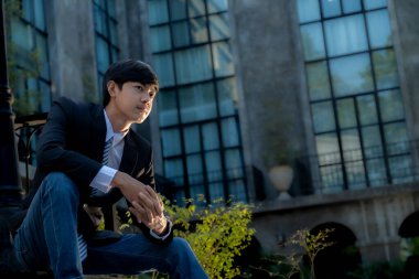 Genç bir işadamı arka planda lüks bir siyah bina ile oturuyor..