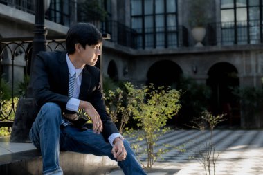 Genç bir işadamı arka planda lüks bir siyah bina ile oturuyor..