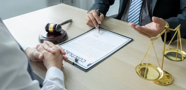 Avukatın eli kalem tutuyor ve ofiste hukuki danışmanlık hizmeti veriyor. Adalet terazisi ve tokmak çekiciyle..