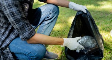 Plastik şişe atıklarını tutan, çöpleri toplayan ve Çevre Dünyası 'ndaki parkta siyah çöp torbasına koyan..