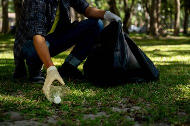 Plastik şişe atıklarını tutan, çöpleri toplayan ve Çevre Dünyası 'ndaki parkta siyah çöp torbasına koyan..