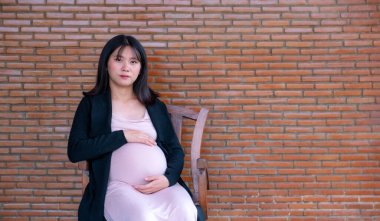 Anne hamile kadın kırmızı tuğlalı arka planda el ele tutuşup bebeğinin doğmasını bekliyor..