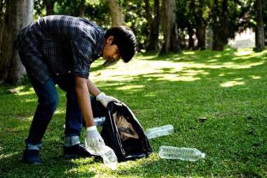 Man Hand plastik şişe atıkları tutuyor, çöpleri topluyor ve Çevre Dünyası 'ndaki parkta siyah çöp torbasına koyuyor..
