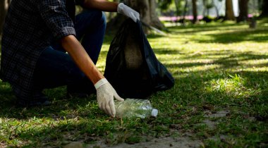 Plastik şişe atıklarını tutan, çöpleri toplayan ve Çevre Dünyası 'ndaki parkta siyah çöp torbasına koyan..