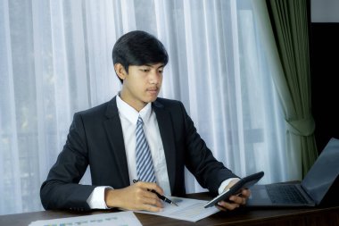 İş adamlarının elinde kalem ve hesap makinesi, dizüstü bilgisayar analizi, zorlu iş hedefleri belirleme grafiği ve merkez ofisteki hedefe ulaşmaya hazır..