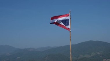Tayland bayrağı rüzgarda dalgalanıyor. Karmaşık bir dağ arka planı var..