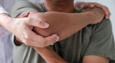 Kadın doktor bir hastanın omzunu uzatarak el tedavisi görüyor. Gerilme egzersizleri ile tedavi.