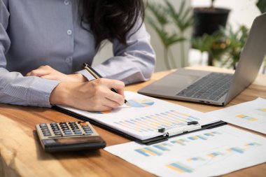 İş kadını ellerinin kalem tutması, iş hedeflerini belirlemek ve yeni hedefe ulaşmayı planlamak için merkez ofisteki bilgisayarı kullanarak grafiği analiz etmesi..