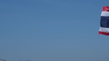 Tayland bayrağı rüzgarda dalgalanıyor. Karmaşık bir dağ arka planı var..