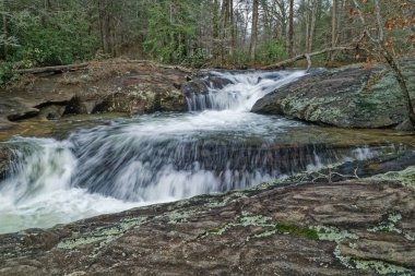 Water rushing downstream over the boulders on the top portion of Dick's creek falls in northern Georgia mountain on a cloudy day at the end of wintertime