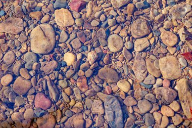 Güneşli bir kış gününde, açık ve sığ bir derede suyun altında çeşitli renkli taş ve kayalar var.