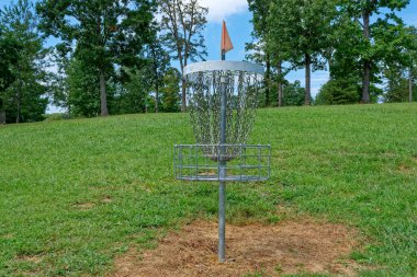 Yazın sonlarında güneşli bir günde, ormanın tepesinde, parkın yakınındaki bir tepede renkli bir bayrak taşıyan bir disk golf sepeti.