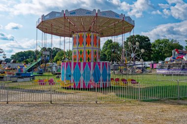 Panayırda eski karnaval gezileri düzenleniyor. Arka planda büyük salıncaklar ve açık güneşli bir yaz gününde panayırda başka geziler.