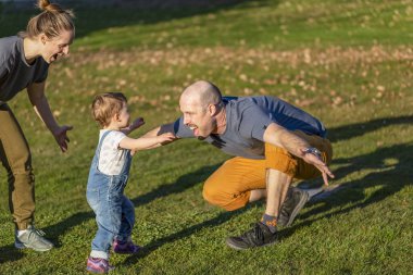 A mother and father play with their toddler daughter in a park; North Vancouver, British Columbia, Canada