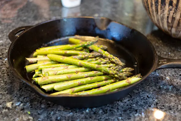 Mutfak tezgahındaki dökme demir tavada kuşkonmaz mızrakları yakın plan.