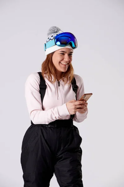 ゴーグル 携帯電話で入力する雪のギアを持つ少女白い背景に笑みを浮かべて — ストック写真