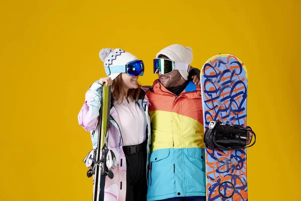 黄色い背景でスノーボードやスキーをしながら雪のゴーグルで見つめ合う笑顔の女の子と男の子 — ストック写真